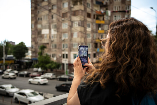 Woman taking smartphone photo of urban city street from balcony, modern travel technology concept