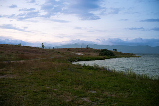 Tranquil Lake Shore at Twilight with Distant Misty Mountains and Overcast Sky
