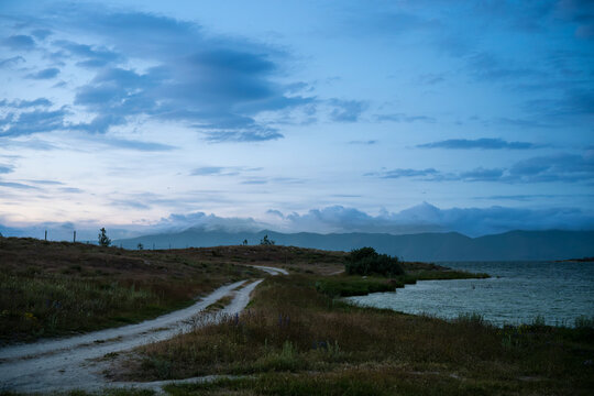 Winding Dirt Road along Coastal Lake in Twilight with Clouds over Mountains