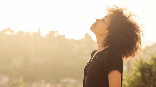 Young woman with curly hair breathing fresh air outdoors at sunset, peaceful girl enjoying warm golden hour light in a beautiful scenic landscape