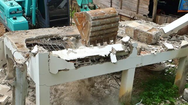 Lampang, Thailand &ndash; September 09, 2026: Close-up of a blue mini excavator bucket breaking down a damaged concrete structure during building demolition work.