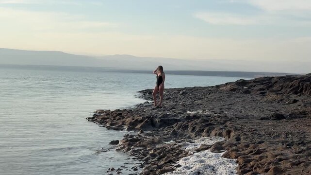 Beautiful footage of a woman standing on the unique mineral rich shoreline of the Dead Sea, one of the world's most extraordinary and iconic natural destinations, Jordan.