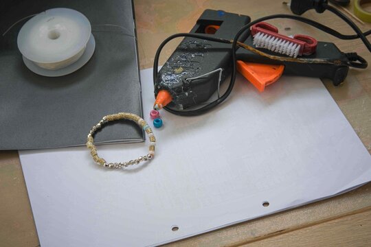 Crafting a simple bracelet using glue gun and beads on a workspace with various tools and materials