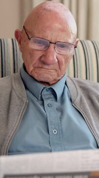 Newspaper, relax and glasses with old man on sofa for obituary check, headlines and reading. Retirement, press release notice and article publication with senior person and tabloid in home for story