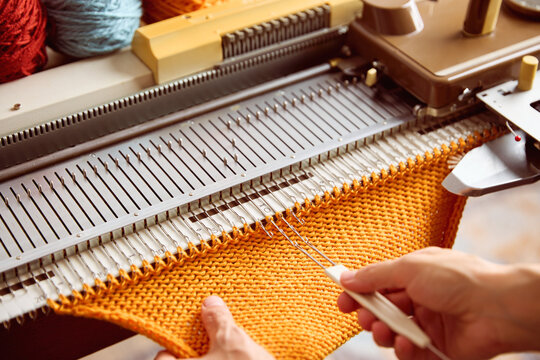 Knitting machine producing orange knitted fabric. Textile crafting process with yarn and knitting equipment.