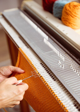 Knitting machine producing orange knitted fabric. Textile crafting process with yarn and knitting equipment.
