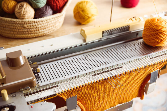 Knitting machine producing orange knitted fabric. Textile crafting process with yarn and knitting equipment.