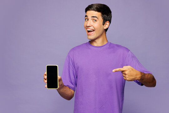 Young Caucasian man wear violet t-shirt casual clothes hold in hand use point finger on mobile cell phone with blank screen workspace area isolated on plain purple background studio. Lifestyle concept