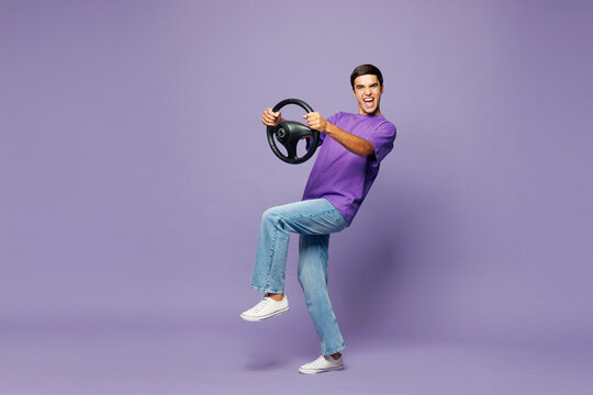 Full body side profile view young shocked fun man he wears lavender t-shirt casual clothes hold steering wheel driving car isolated on plain pastel light purple background studio. Lifestyle concept.