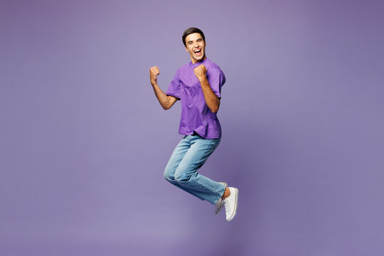 Full body young cool Caucasian man he wears violet t-shirt casual clothes jump high do winner gesture clench fist isolated on plain pastel light purple background studio portrait. Lifestyle concept.