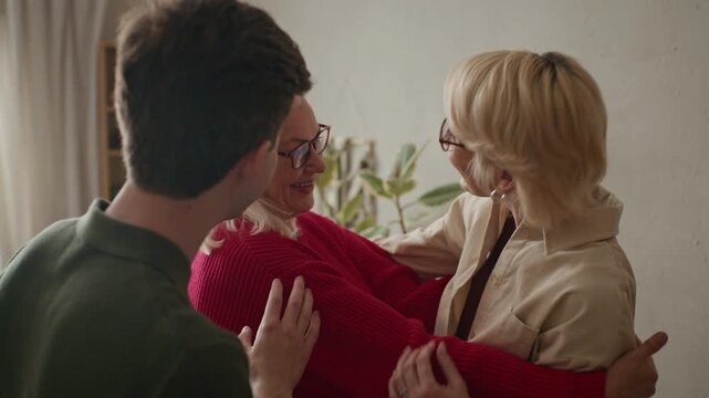 Senior Caucasian woman hugging young adult grandson and middle aged daughter while talking and laughing during family visit. Video is ideal for senior care or family insurance marketing