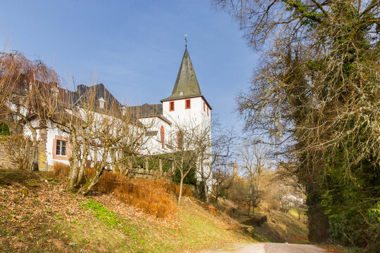 Historic white church on a tree lined hillside slope in Kronenburg, Germany