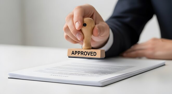 Close-up of a hand holding an 'APPROVED' stamp over an official document, symbolizing business authorization and consent.
