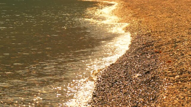 Summer sea surf washes onto a pebbled beach during a golden hour sunset. High-angle static shot.