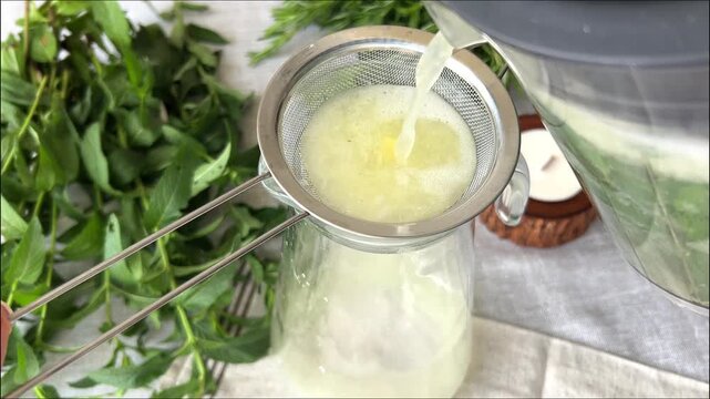straining homemade summer lemonade through sieve with mint leaves and fresh ingredients showing beverage preparation process concept of healthy drinks cafes hospitality recipes and culinary content