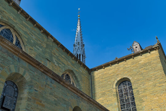 The yellow stone exterior of a church or cathedral stands against a clear blue sky, featuring arched windows and a tall, intricate spire - Soest, Westphalia, Germany