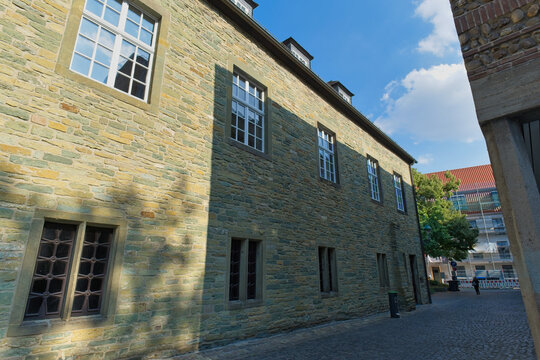 A historic building, constructed from light-colored stone, stands prominently on a narrow cobblestone street under a bright blue sky - Soest, Westphalia, Germany