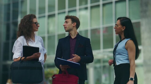 Three business professionals conduct an outdoor meeting, discussing important corporate matters. A team of colleagues collaborates on strategy in a modern urban setting.