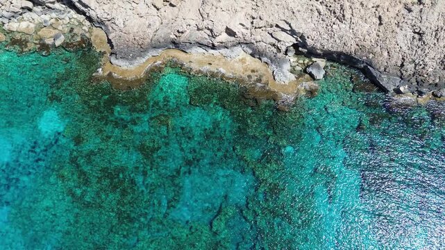 Top down aerial view of turquoise sea water splashing against rocky coastline at Cape Greco, Cyprus