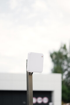 White outdoor RFID antenna scanner for automated vehicle access control system. Long range reader for parking barrier gate at modern residential complex.