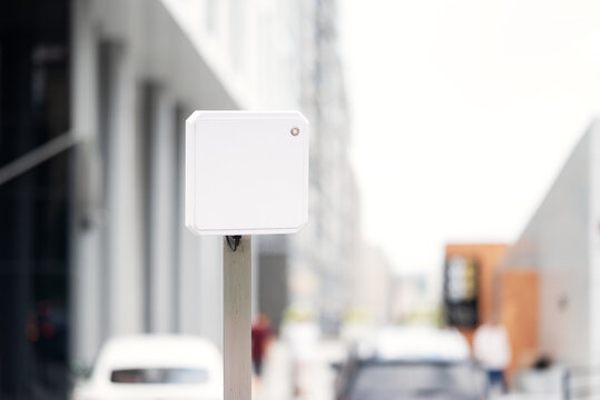 White outdoor RFID antenna scanner for automated vehicle access control system. Long range reader for parking barrier gate at modern residential complex.
