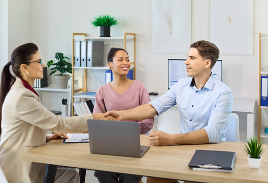 Advisor couple handshake in consultation meeting agreement. Smiling partners sign papers with advisor in office, confirming trust, clarity and support. Strong deal and partnership concept.