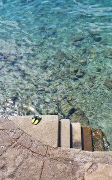 Stone and concrete stairs lead directly into crystal clear turquoise sea water with flip flops left on the edge.