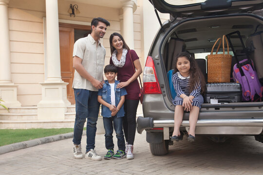 Family standing beside open boot of parked car to go on vacation
