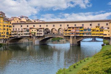 Fototapeta premium The Ponte Vecchio bridge in Florence showcases its colorful buildings and shops reflecting in the tranquil waters Arno river.