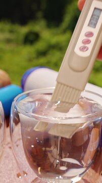 Vertical video. Person Comparing Water Samples With a Digital TDS Meter, Measuring Total Dissolved Solids to Detect Clean and Contaminated Drinking Water, Close Up, Water Safety