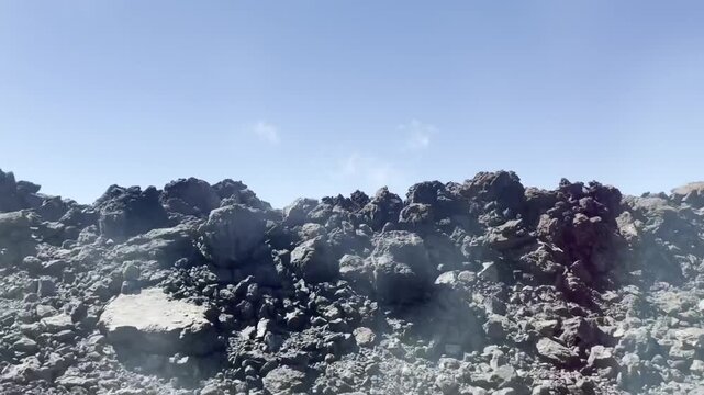 Dynamic side window view of driving car passing frozen black lava field in Tenerife. Barren volcanic rock formations, rough stone badlands under bright blue sunny sky. National park scenic roadtrip.