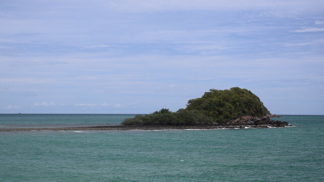 The image depicts a small, lush green island with dense vegetation, situated in the middle of a calm, turquoise body of water