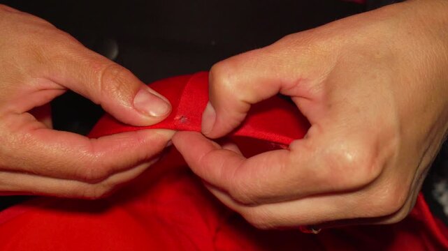 Seamstress folds red fabric edges carefully, preparing for accurate stitching at a workstation. Extreme close-up shot focused on precise finger movements.