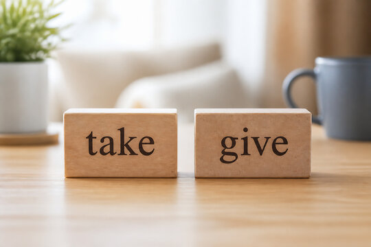 Two wooden blocks with the words take and give are placed on a light wooden table in a bright indoor setting.