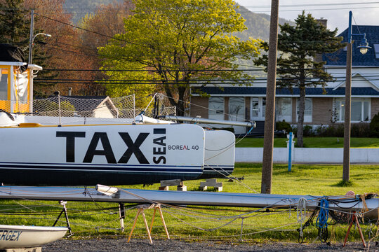 Gaspesie, Canada, 31 May 2026 : A white catamaran named TAX SEA BOREAL  is dry-docked on land near residential buildings.