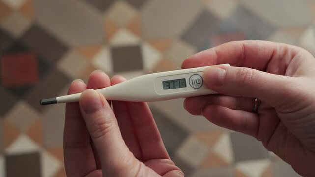 Close-up of hands holding a digital thermometer displaying a body temperature of 37.1 on the screen. Concept of health monitoring and fever check. High quality 4k footage