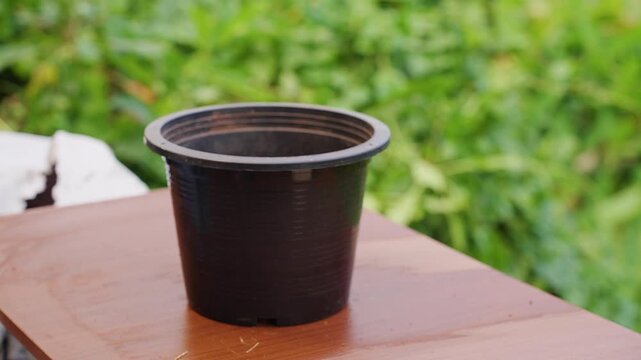 Gardener Wearing Protective Gloves Adds Coconut Husk to a Black Plastic Pot, Creating Natural Drainage for Growing Plants Outdoors