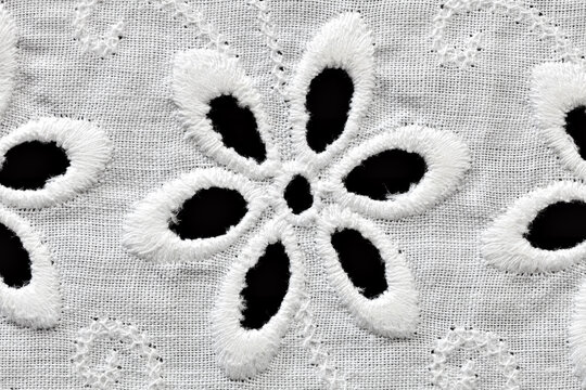 Extreme close-up macro of a single six-petal cutwork flower embroidered on white cotton sangallo fabric, isolated on black background.