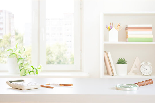 Stylish workplace white table top with stationery, calculator and magnifier on blurred window sill background