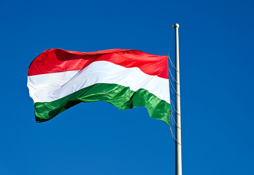Hungarian national flag flying high and waving in the wind. red, white and green stripes. shiny silk fabric. blue sky background. metal flag pole. patriotism concept. national symbol.