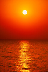 Fototapeta premium Intense vibrant red and orange sunset over quiet sea horizon with bright sun reflection on water.
