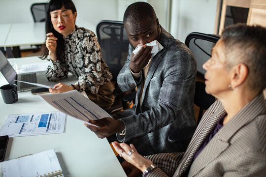Business colleagues in office meeting as coworker blows nose