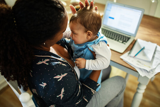 Young mother comforting baby while working from home at kitchen table