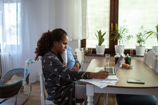 Mother paying bills at home while holding baby