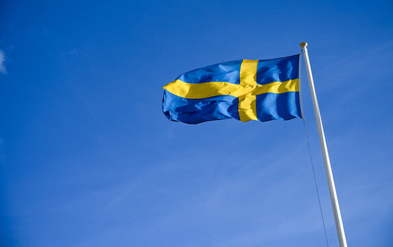 National flag of Sweden waving on flagpole. Official Swedish national flag against blue sky.