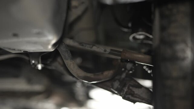 A mechanic's hand checking a car steering tie rod underneath a vehicle.