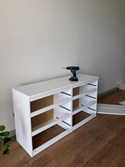 DIY furniture assembly in a modern apartment. White cabinet being assembled with a cordless drill during home renovation and interior furnishing. © leroy