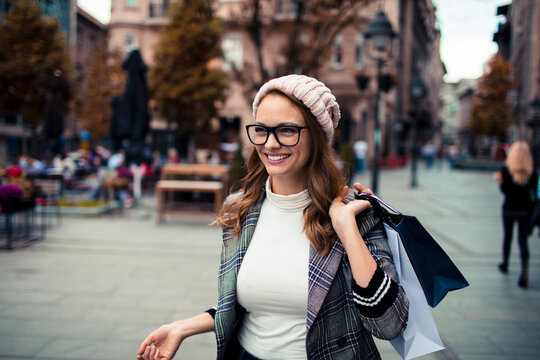 Smiling young woman with shopping bags walking on city street in autumn