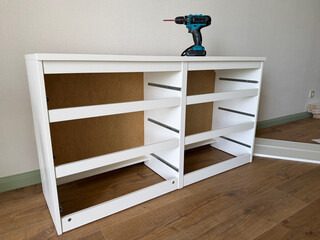 DIY furniture assembly in a modern apartment. White cabinet being assembled with a cordless drill during home renovation and interior furnishing. © leroy