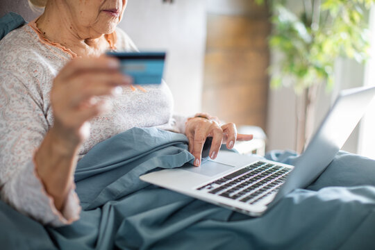 Senior woman shopping online with credit card in bed at home